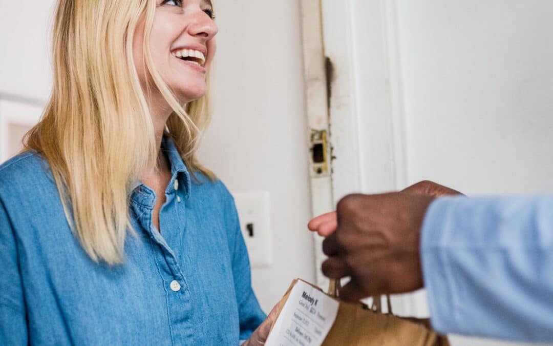 Glimlachende vrouw die een pakketje in ontvangst neemt aan de deur bij een online bestelling