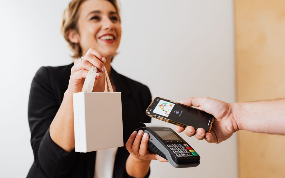 Verkoopster overhandigt een tas terwijl een klant contactloos betaalt met een smartphone bij de kassa