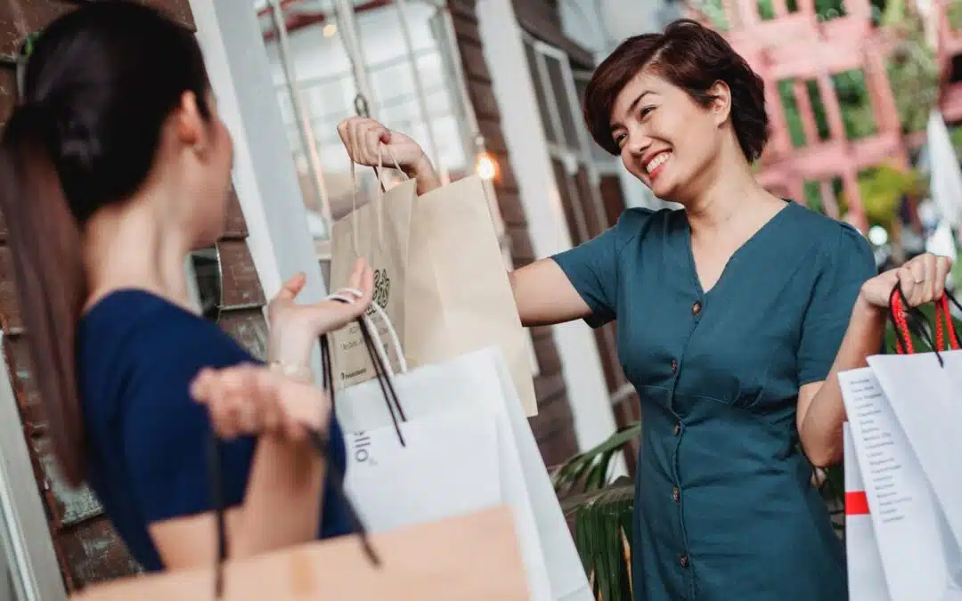Twee vrouwen wisselen lachend cadeautassen uit tijdens het winkelen