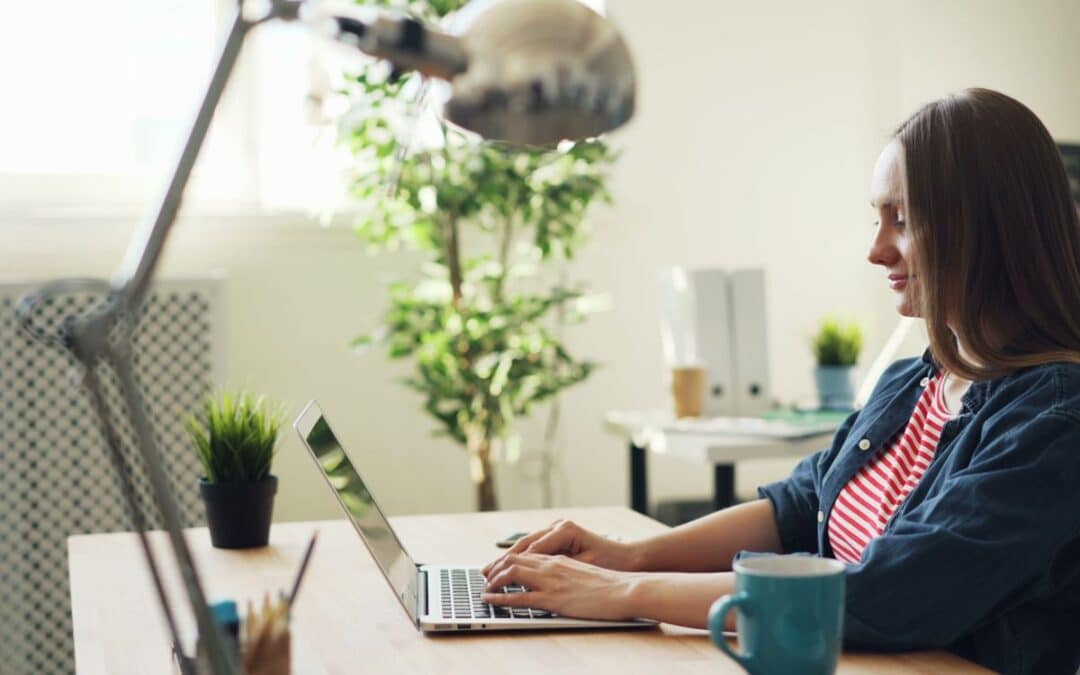 Vrouw werkt glimlachend op een laptop in een modern kantoor met planten, terwijl ze productteksten schrijft voor haar webshop