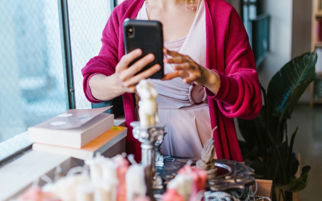Ondernemer maakt met een smartphone een foto van handgemaakte kaarsen bij het raam voor de eigen webshop