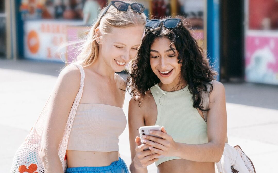 Twee vriendinnen bekijken lachend een product op een smartphone tijdens het winkelen op straat