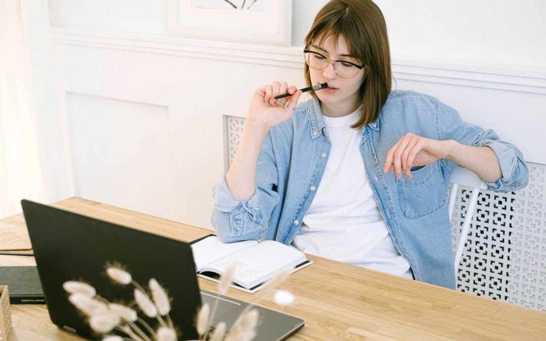 Webwinkelier aan een houten bureau denkt na met een pen in de hand, naast laptop en notitieboek