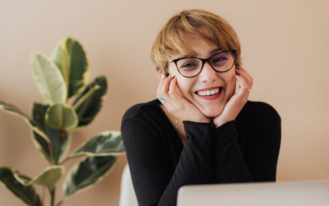 Lachende vrouw met bril achter haar laptop, een tevreden klant van een webshop