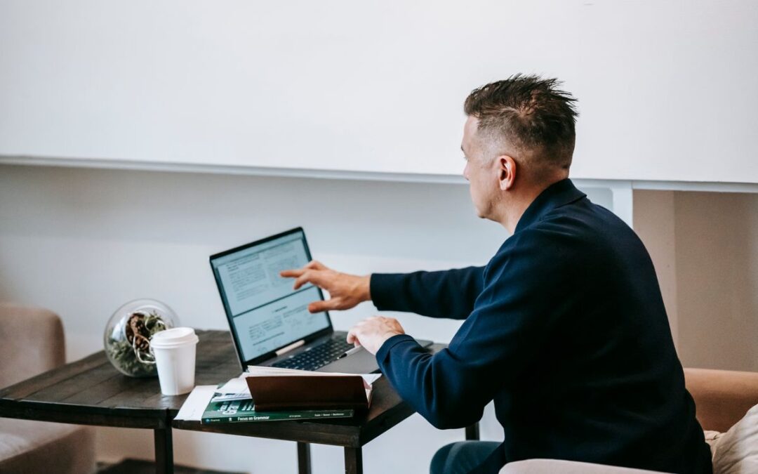 Man werkt aan een laptop op een thuiswerkplek met een kop koffie en notities